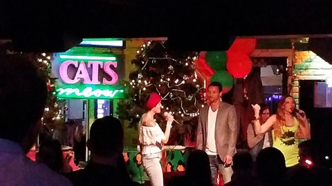 Singers performing on a small bar stage under a neon sign