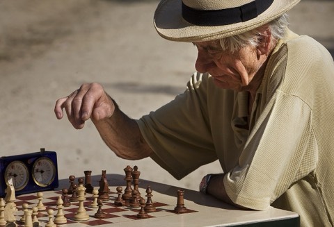 An older man moving a piece during an outdoor game of chess