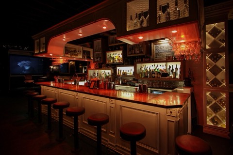 A long, warmly lit cocktail bar with stools and shelves of bottles