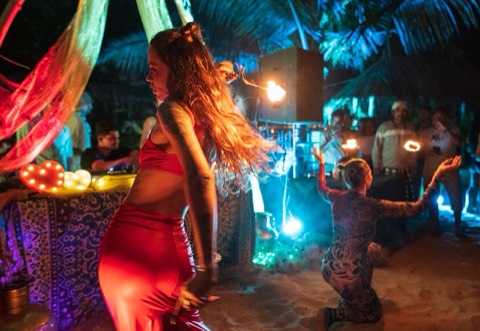 A fire dancer performing at a night beach party, lit by flames and colored lights