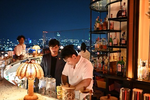 Bartenders mixing drinks at a rooftop bar with city lights behind them