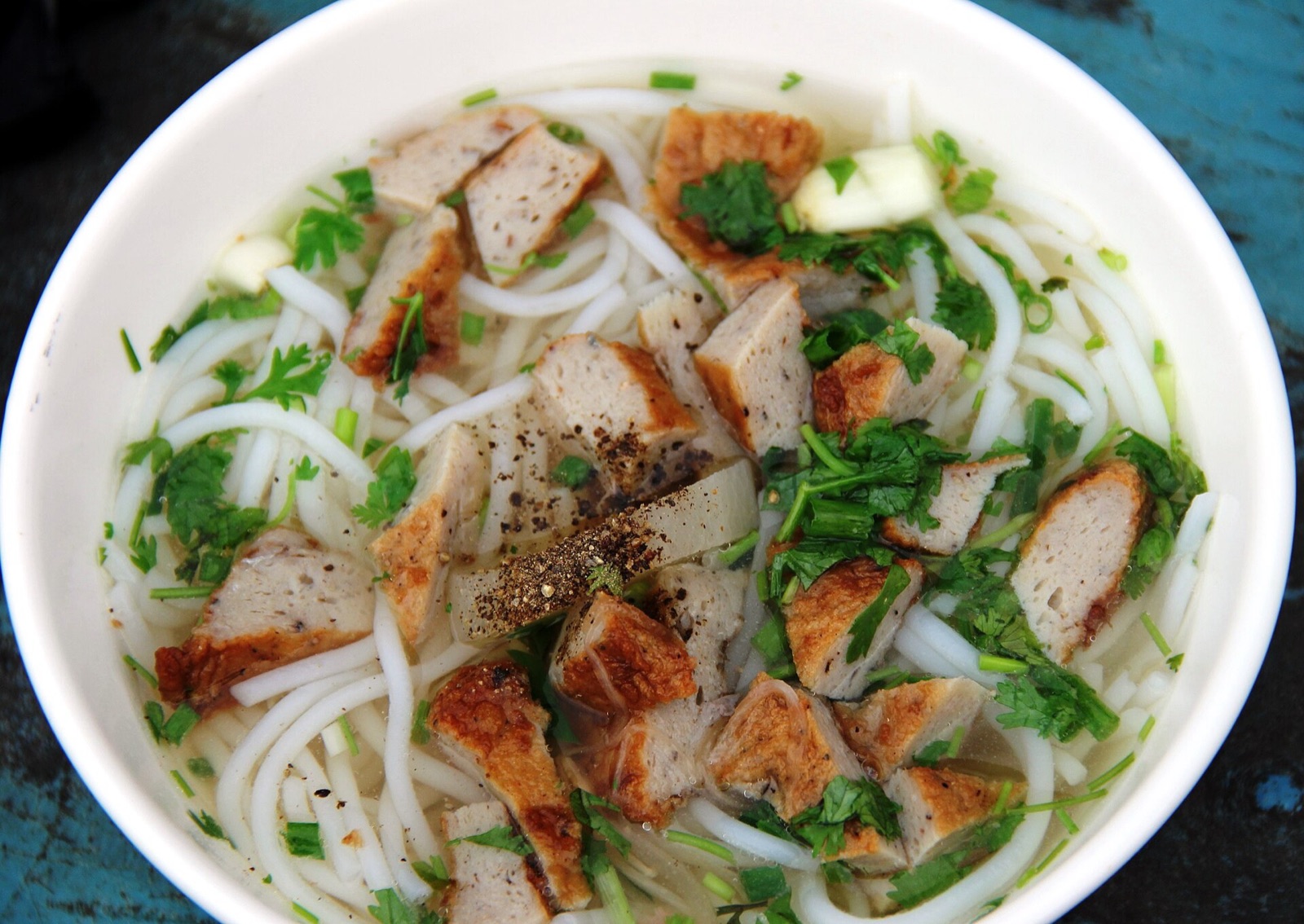 A bowl of bun cha ca with rice vermicelli, slices of fish cake, herbs and black pepper in a light broth