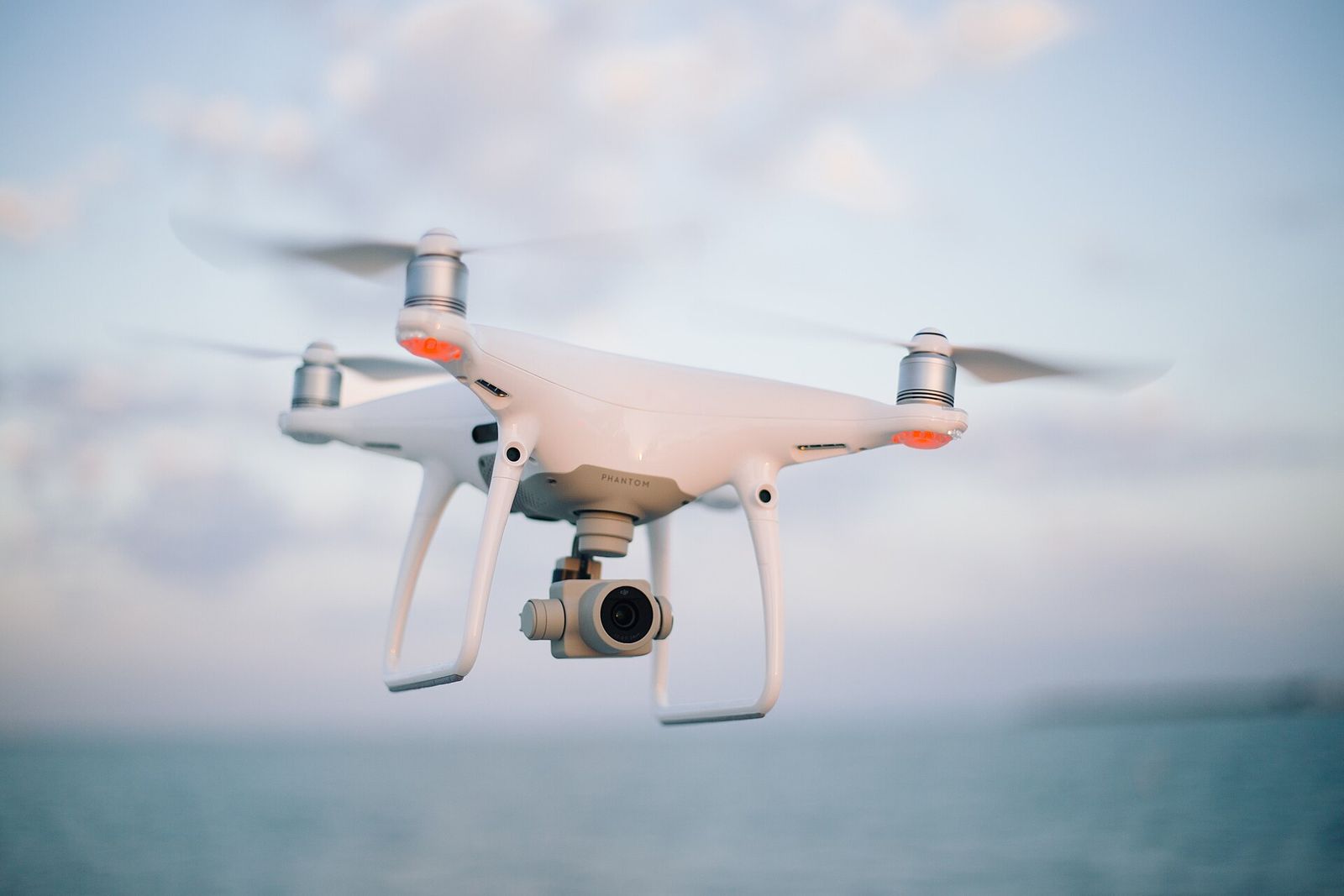A white four-rotor camera drone hovering in the air