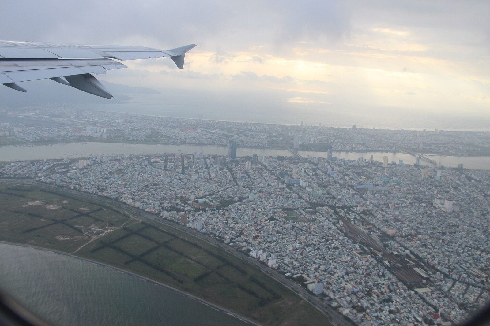Hazy aerial view of Da Nang's urban grid and coastline seen from an airplane window