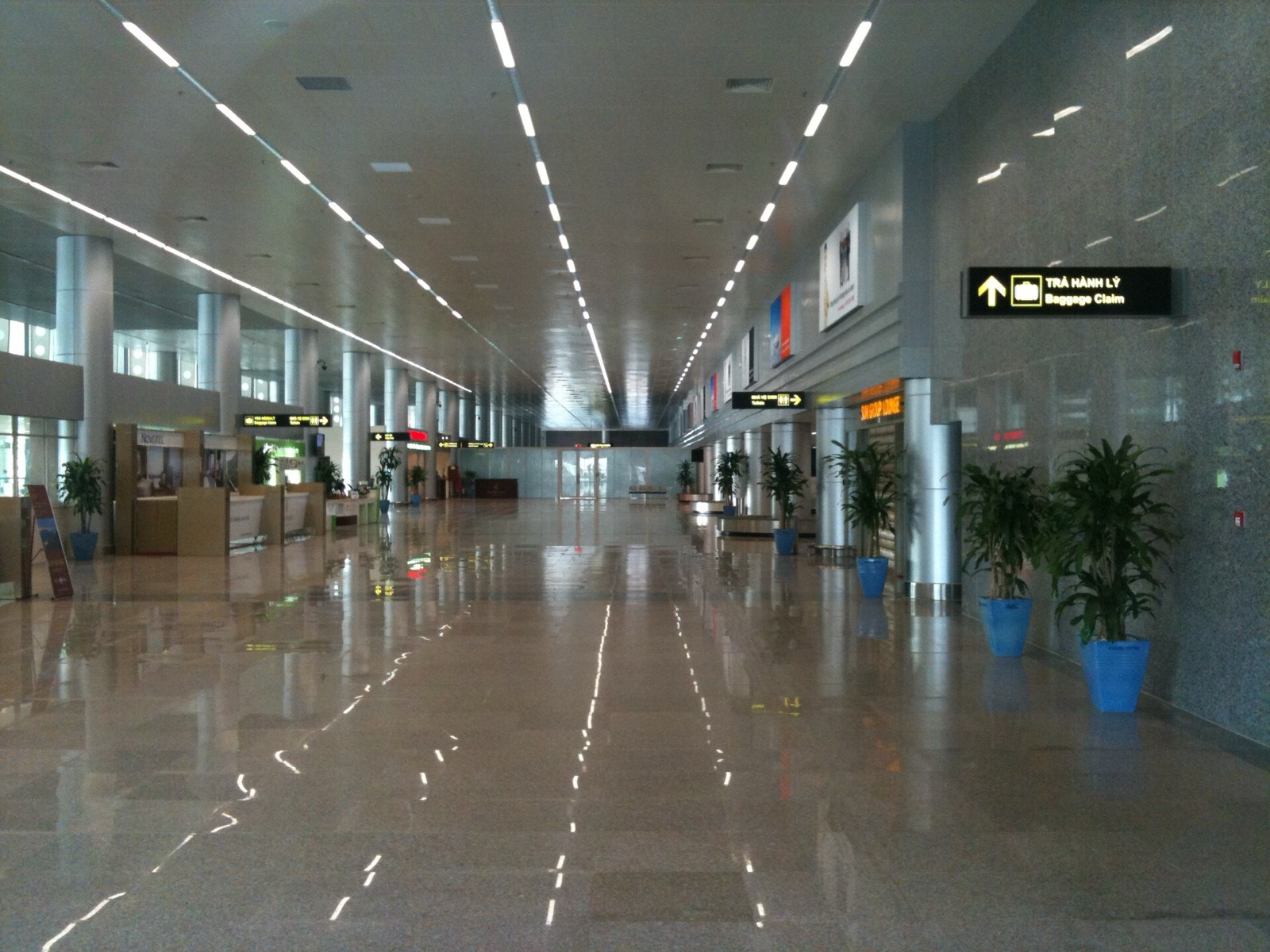 A long, bright arrivals hall at Da Nang International Airport with a polished floor, potted plants and baggage claim signs