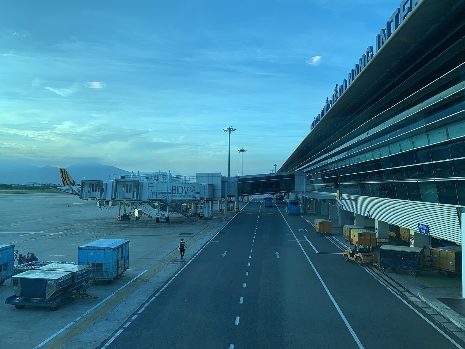 The glass-fronted international terminal at Da Nang International Airport with jet bridges and a parked aircraft on the apron under a blue sky