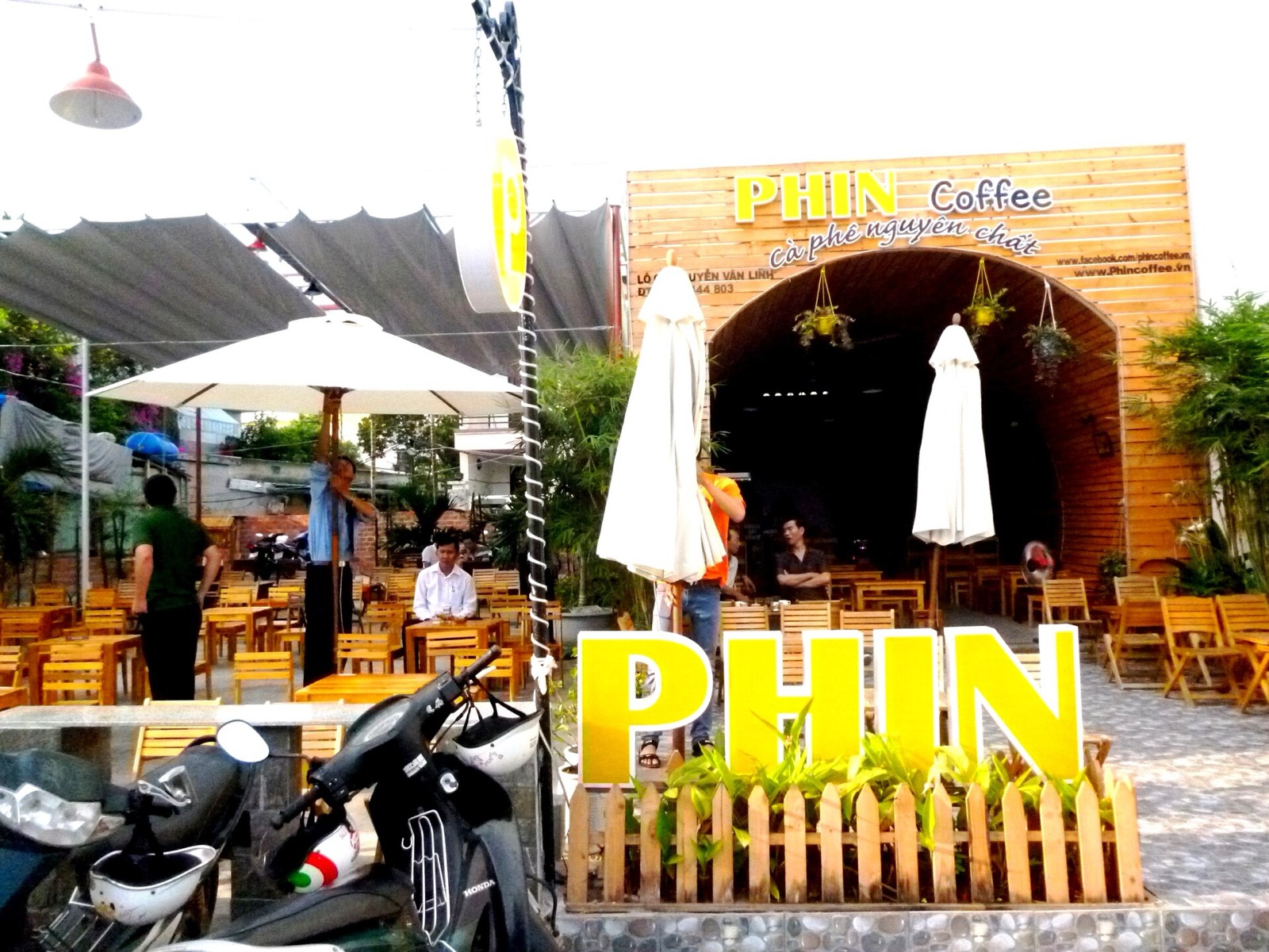 The open front of a Da Nang café with a yellow PHIN sign, umbrellas, wooden tables and a few customers seated inside