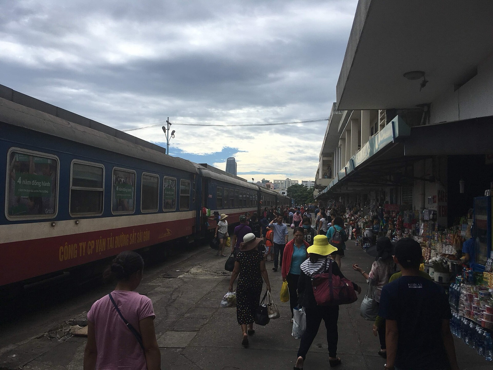 Passengers walking along a platform at Da Nang railway station beside a blue and red Vietnam Railways passenger train