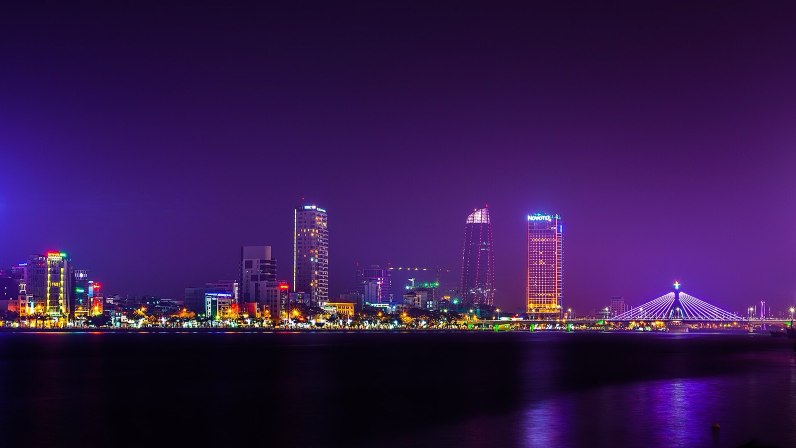 Da Nang's riverfront skyline lit up at night, with high-rise towers and a bridge reflected in the Han River