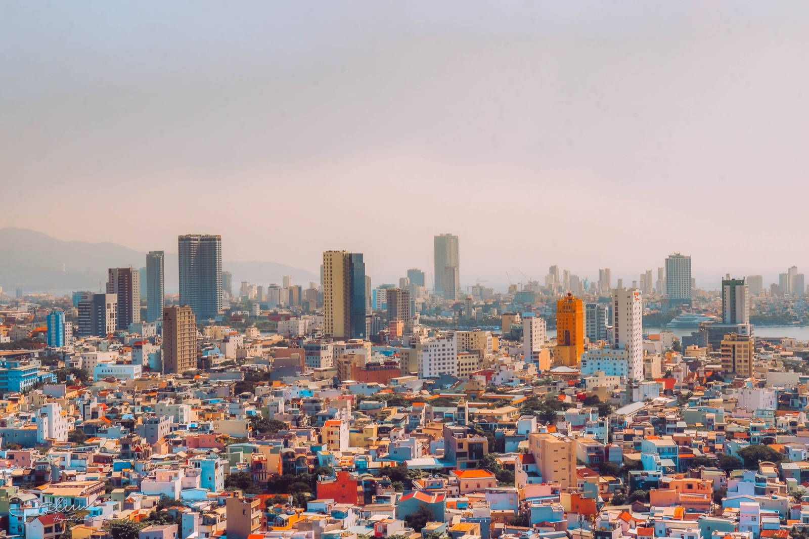 Dense rooftops of low-rise houses stretching toward high-rise towers in central Da Nang under a pale sky
