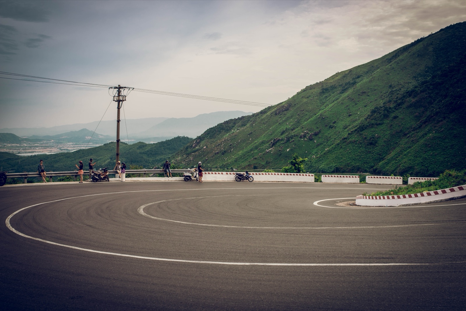 An empty mountain road curving below steep green hills under an overcast sky near Da Nang