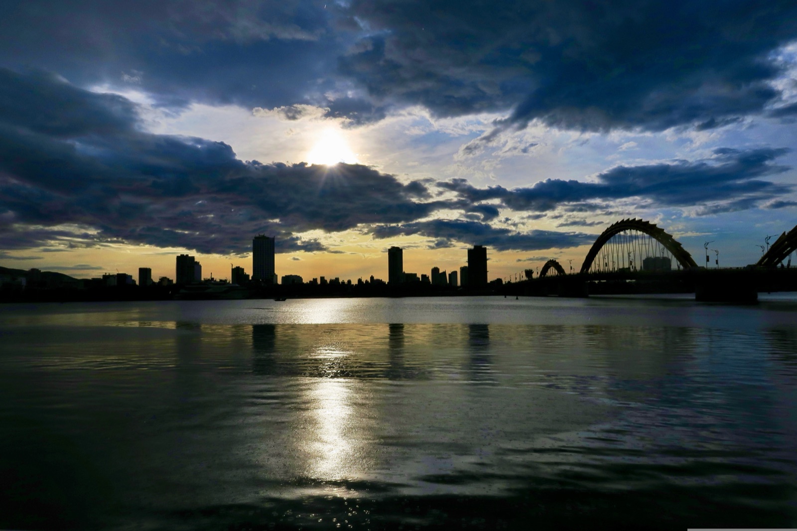 Dark storm clouds over the Han River with the city skyline and a bridge in silhouette