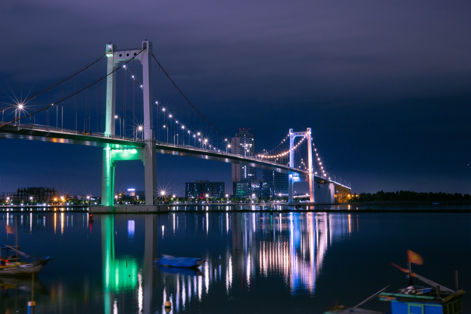 The Thuan Phuoc suspension bridge lit up in blue and white at night over calm water in Da Nang