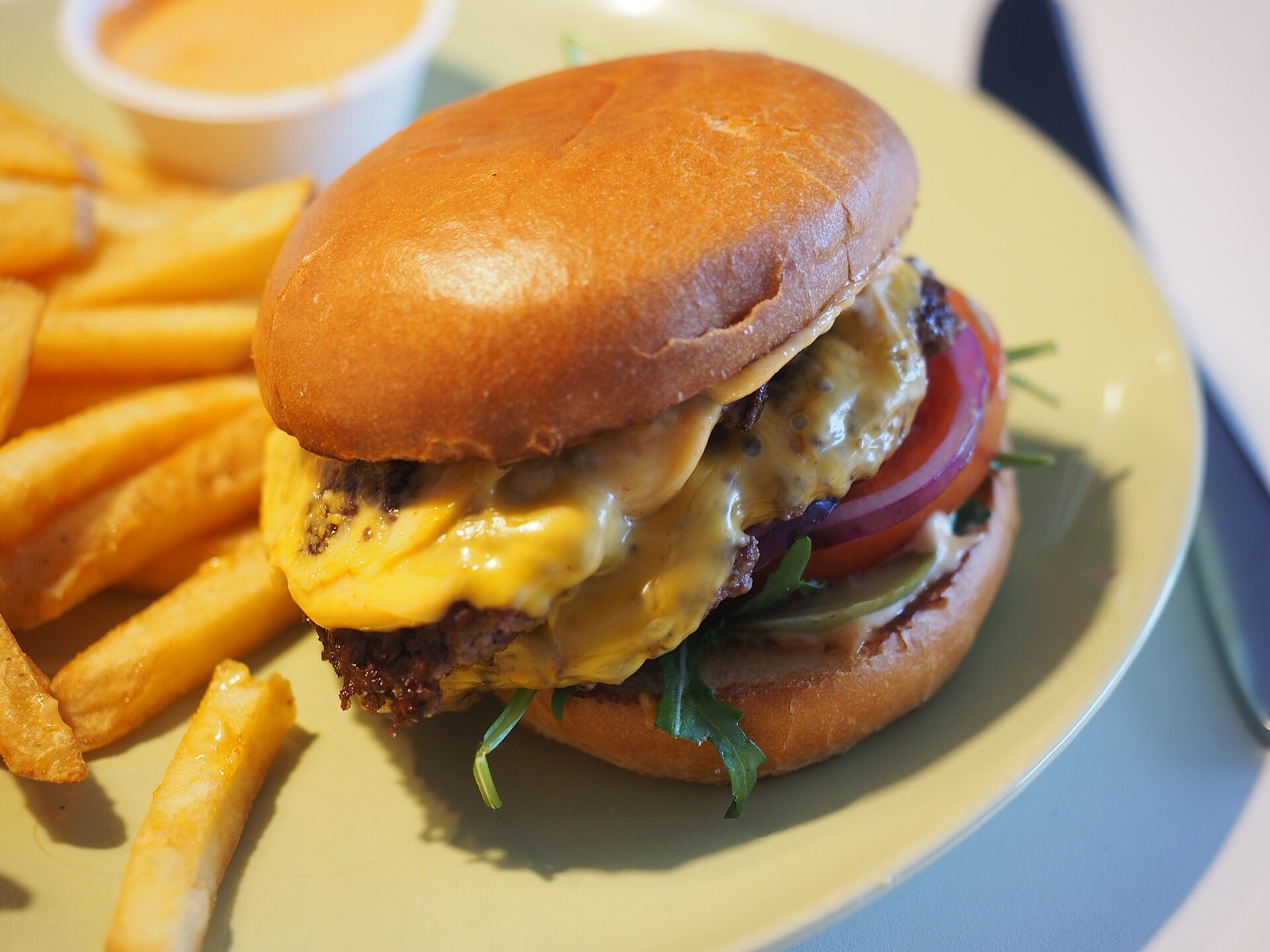 A double smash burger with melted cheese, tomato and greens in a toasted bun, with fries on the side