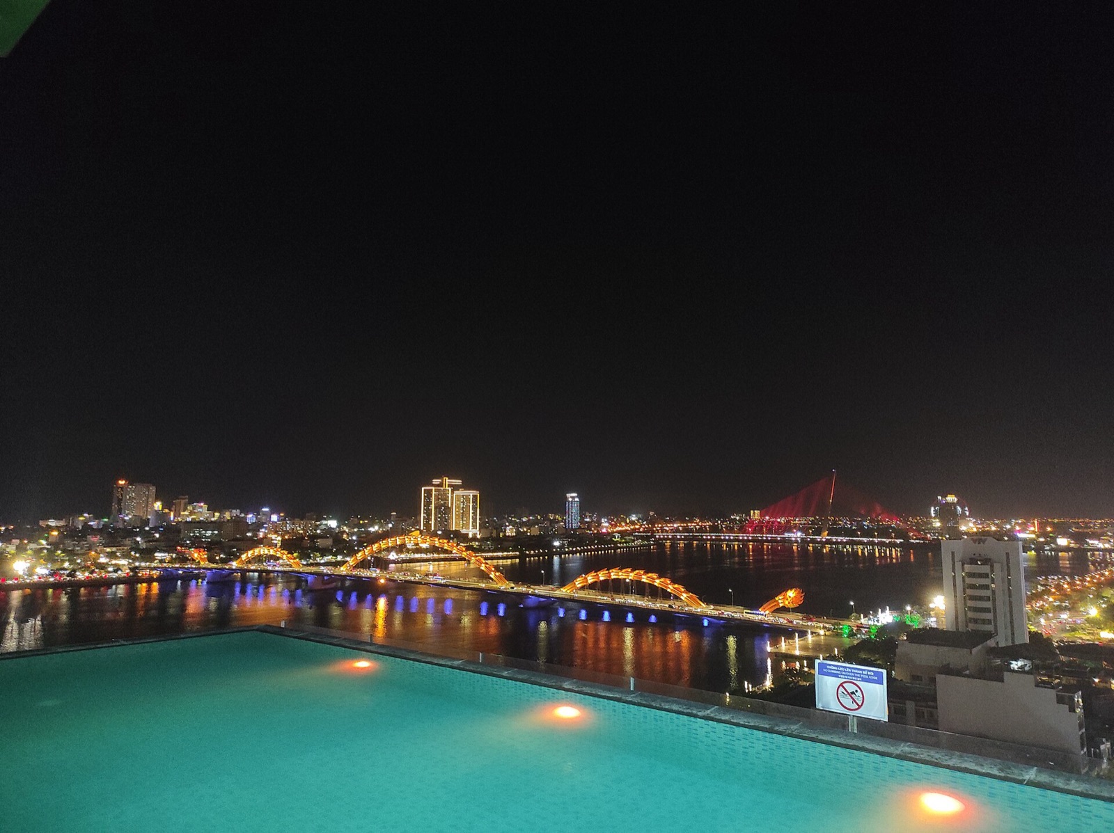 The lit-up Dragon Bridge and Han River at night seen from a rooftop pool terrace