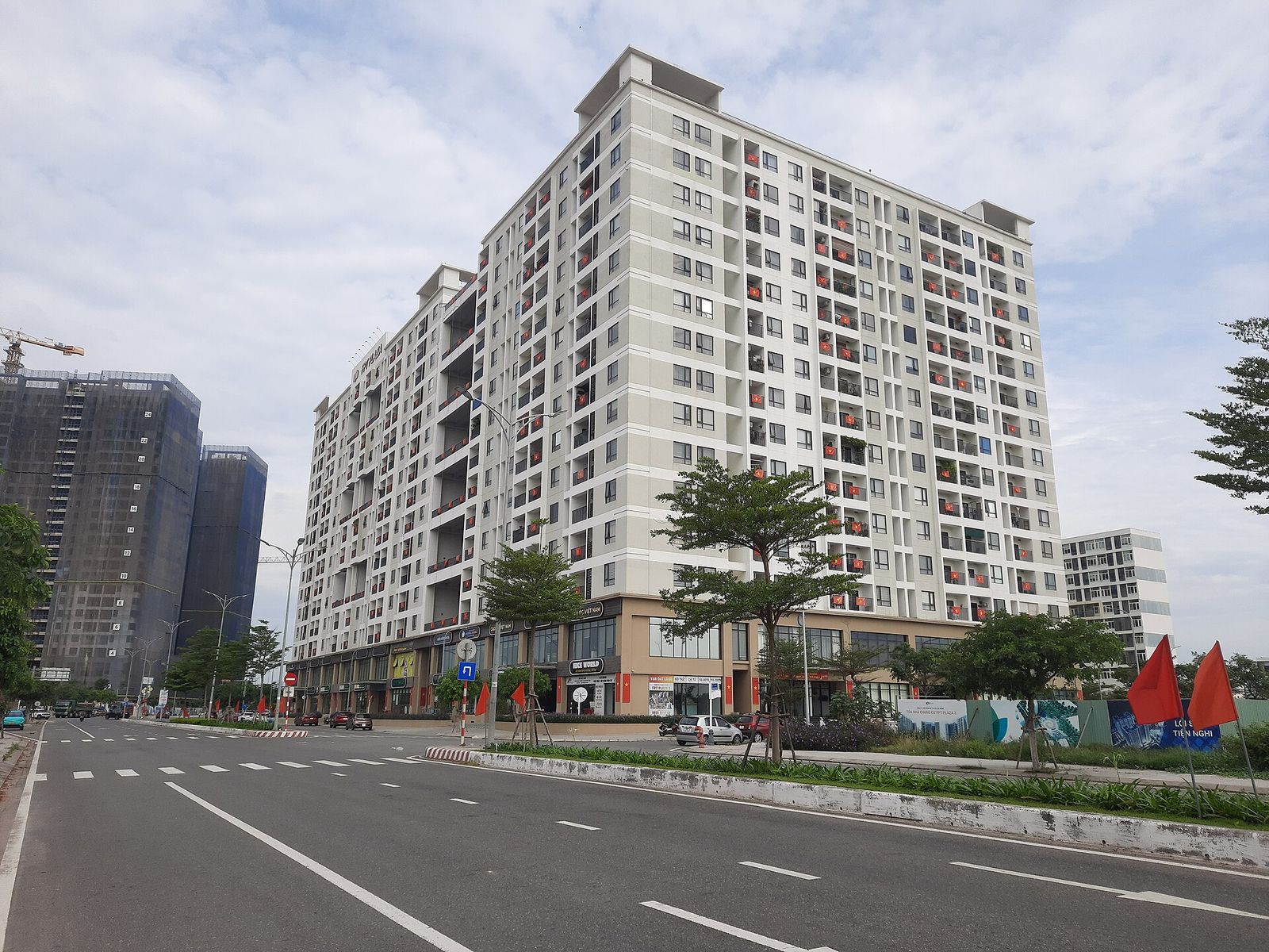 A white high-rise apartment block beside a wide, empty road under a cloudy sky