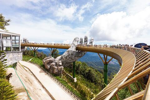 The Golden Bridge at Bà Nà Hills, a curved footbridge held up by two large stone-textured hands, with tourists walking along it