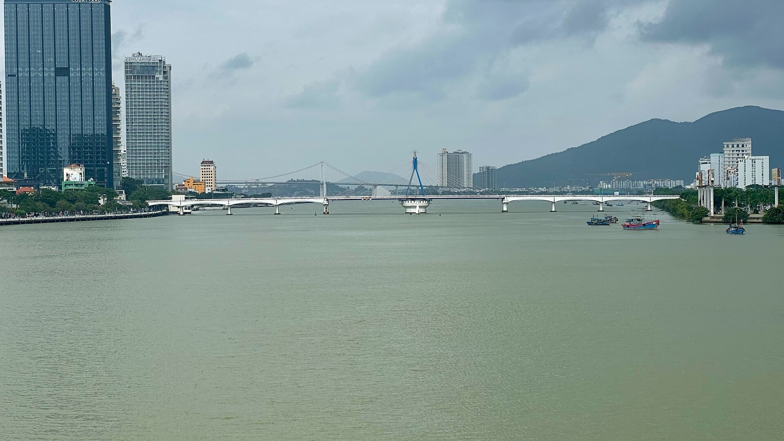 The wide Han River in Da Nang with the low Han River Bridge crossing it, towers on the left bank and the Son Tra mountain in the distance