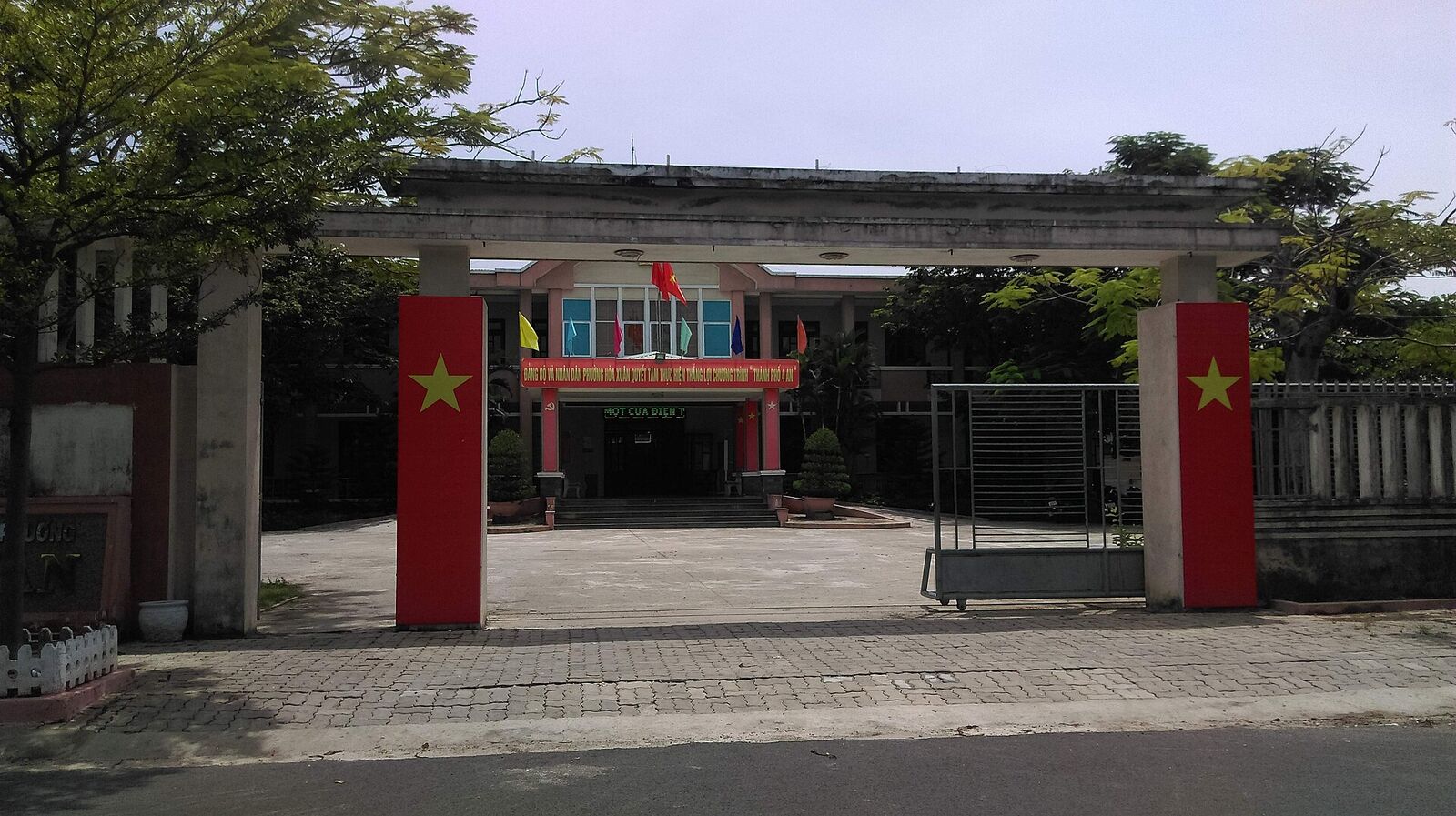 The gated entrance and two-storey People's Committee office of Hòa Xuân ward, with red flag panels on the gateposts