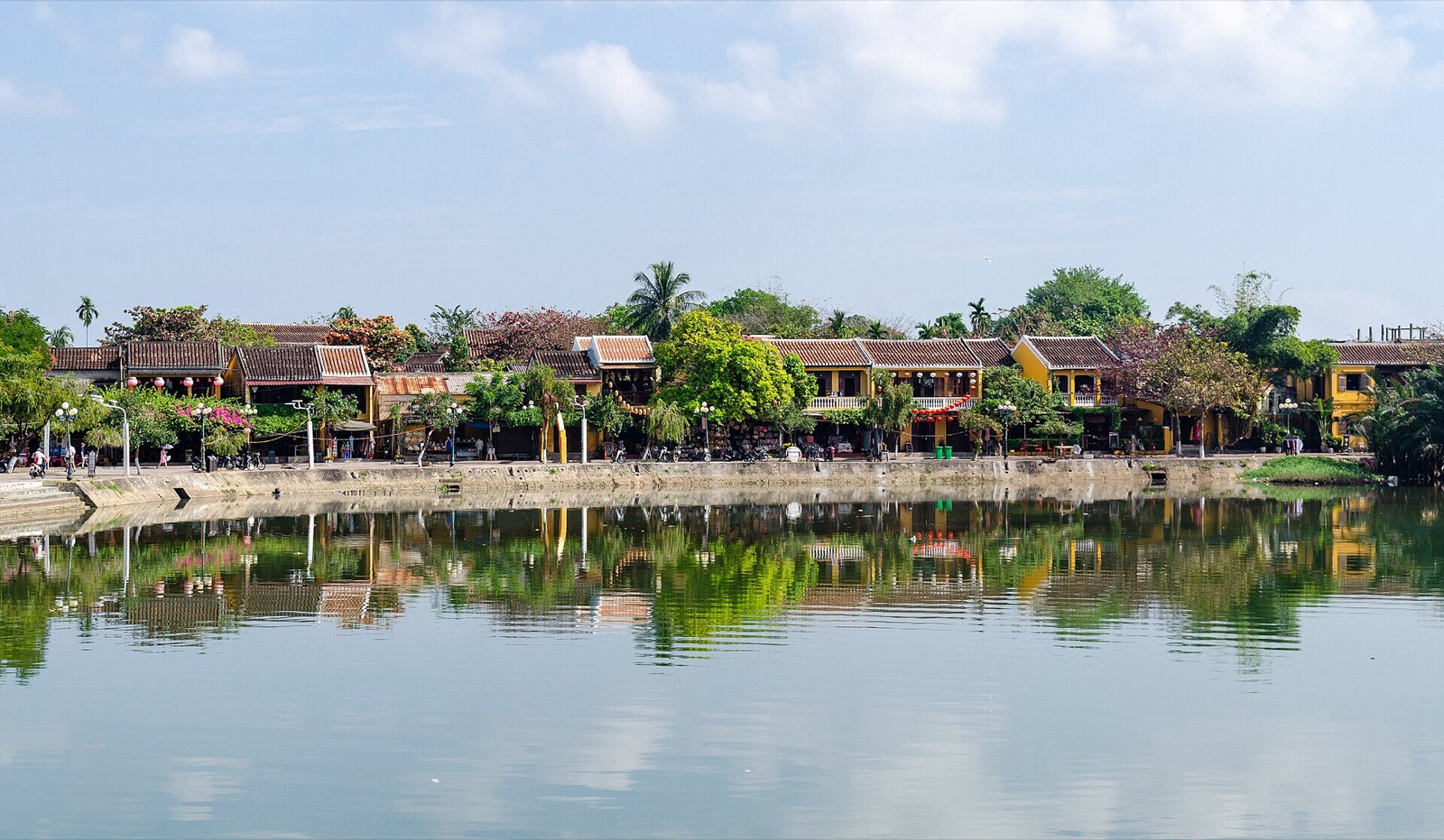 Low yellow shophouses and trees in Hoi An's ancient town reflected in still water under a pale sky