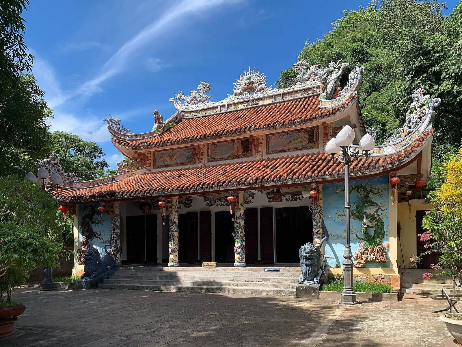 Tam Thai Pagoda on Thuy Son, with a curved tiled roof decorated with dragons, set against green trees and a blue sky