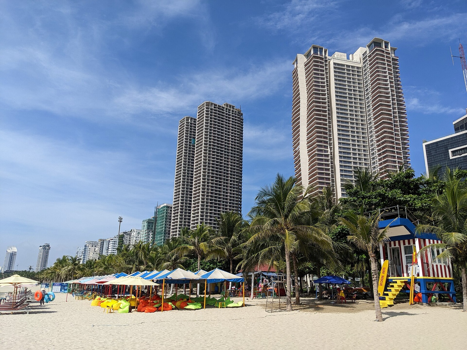 High-rise apartment towers behind the palm trees and beach umbrellas of My Khe Beach on a sunny day