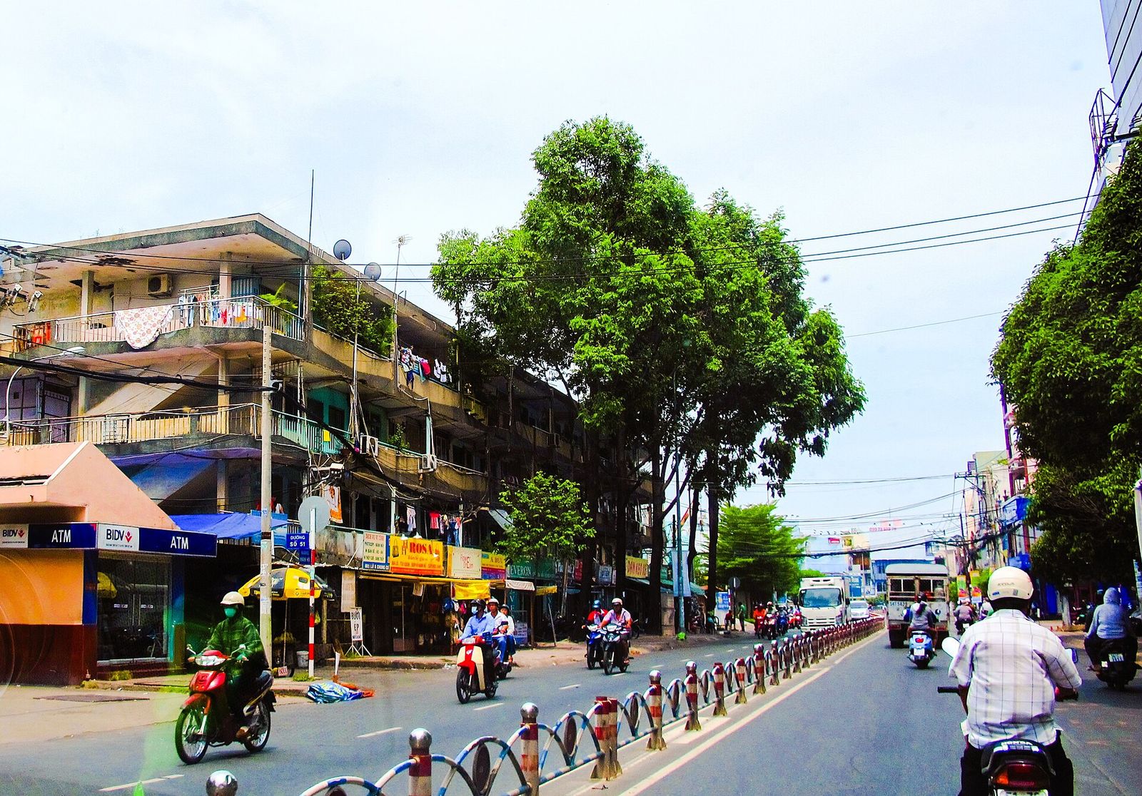 A weathered multi-storey apartment block with balconies above shopfronts on a busy street