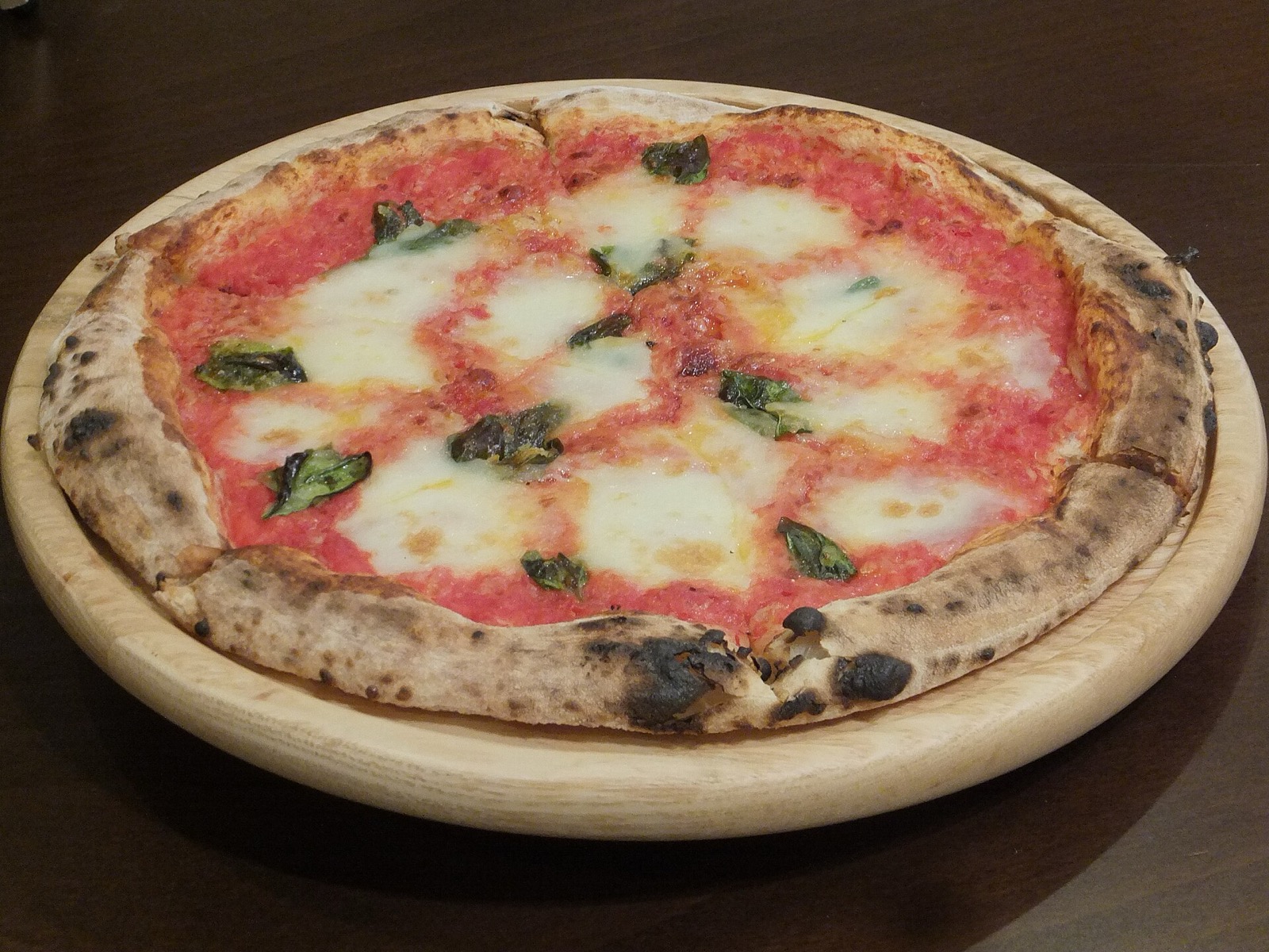 A round Neapolitan-style margherita pizza with a puffy, charred crust, tomato, mozzarella and basil on a plate