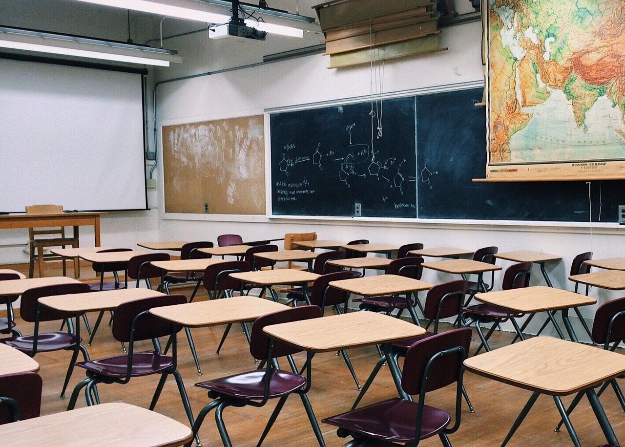 Stock photo of an empty classroom with rows of desks, a chalkboard and a wall map