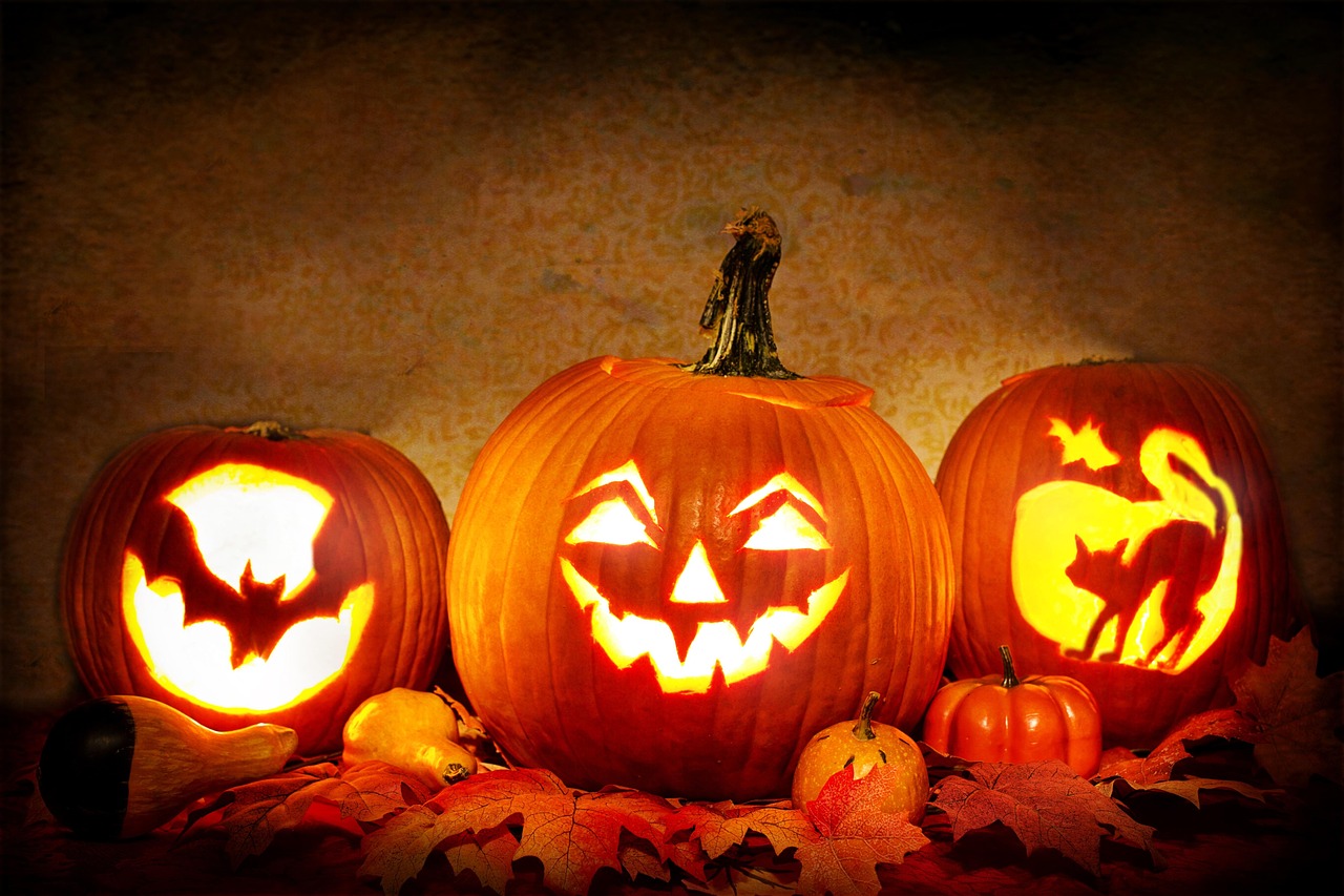 Three carved pumpkins with glowing faces among autumn leaves