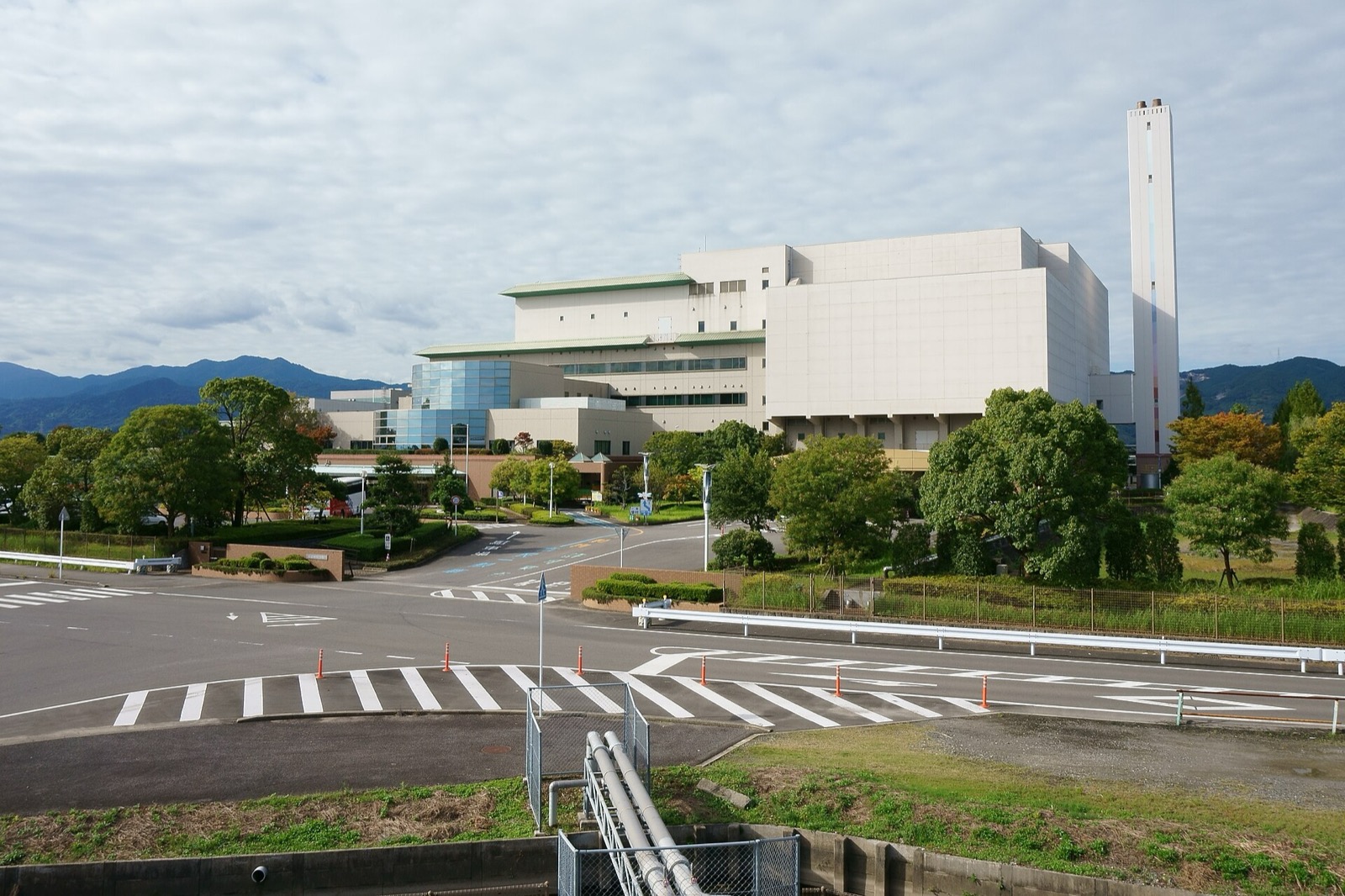 A modern waste incineration plant with a tall chimney and a pipeline in the foreground