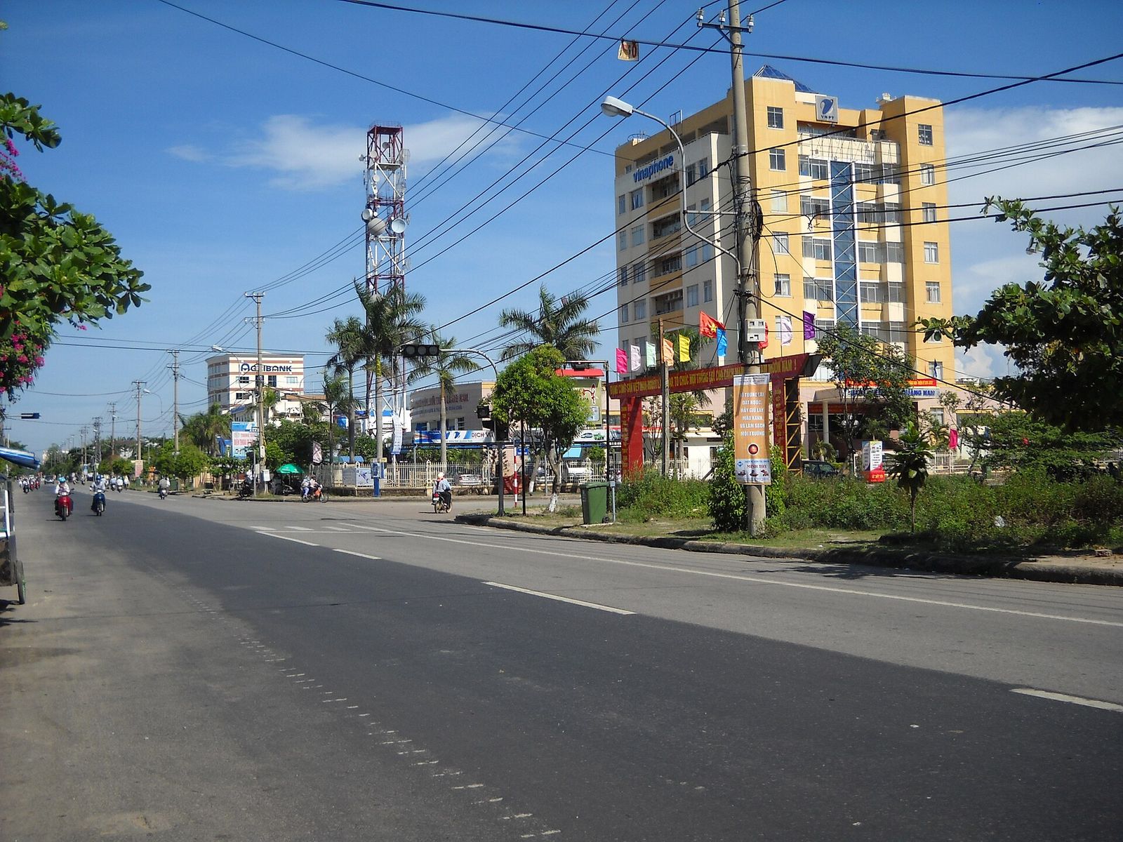 A wide, quiet street with a median strip, palm trees and a yellow building under a blue sky