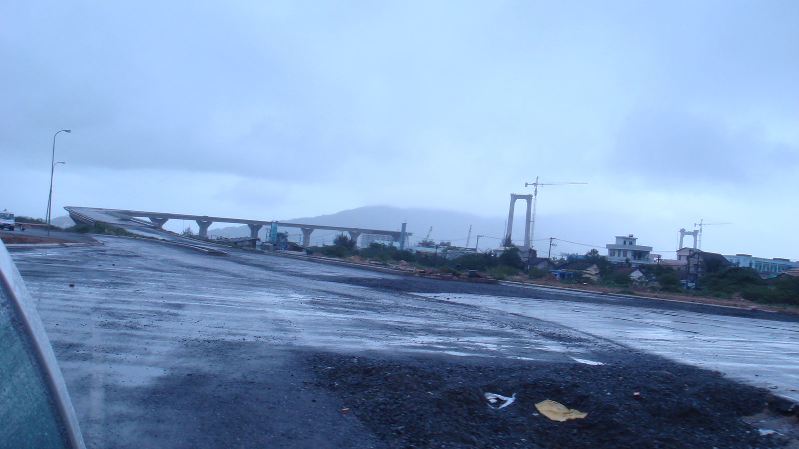 An unfinished suspension bridge with its towers rising over the river under a grey sky