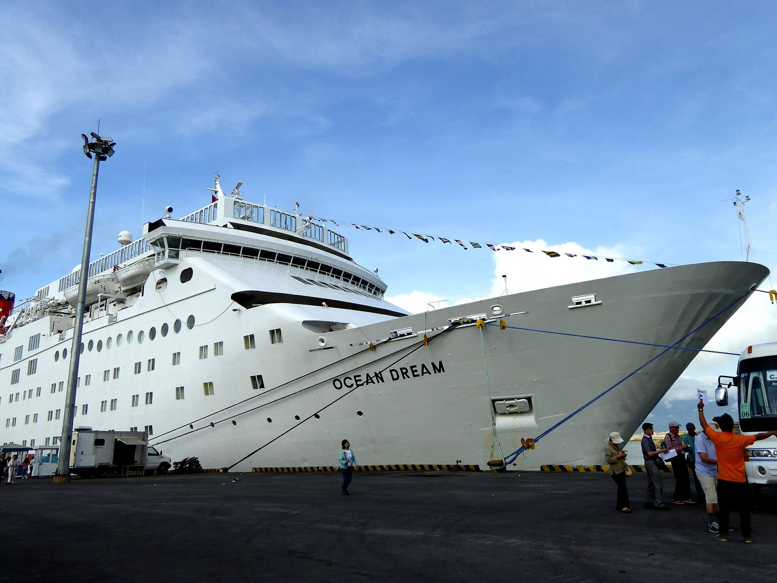 A large white cruise ship moored at the quay of Tien Sa Port in Da Nang under a blue sky, with a few people on the dock