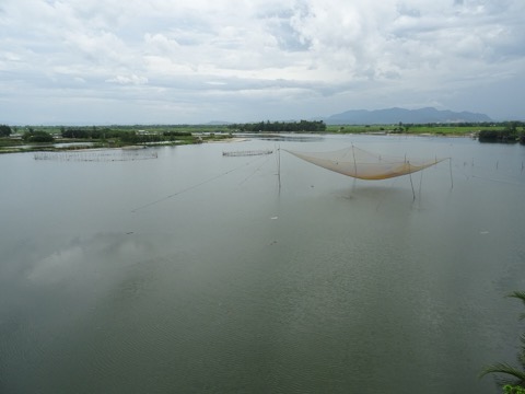 The broad, calm Truong Giang River with fishing nets on poles and low green banks under a grey sky