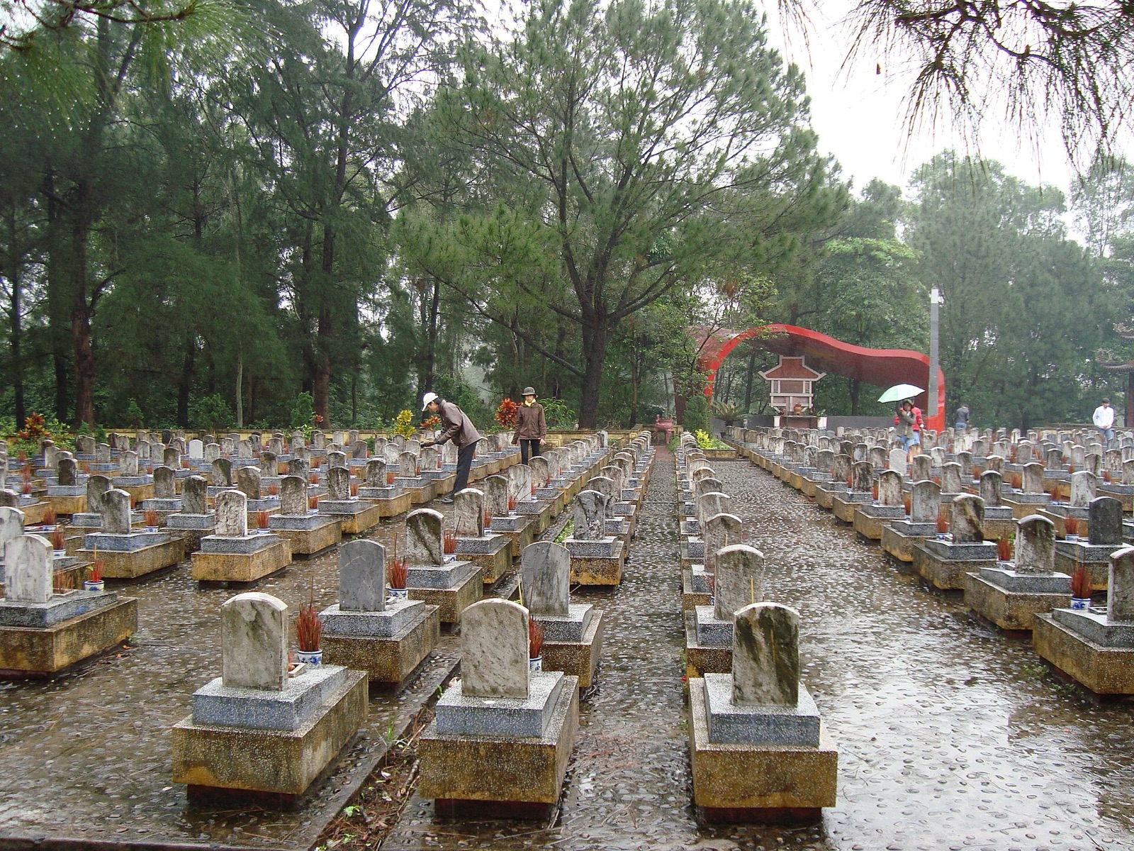 Rows of white headstones in a national martyrs' cemetery shaded by tall trees